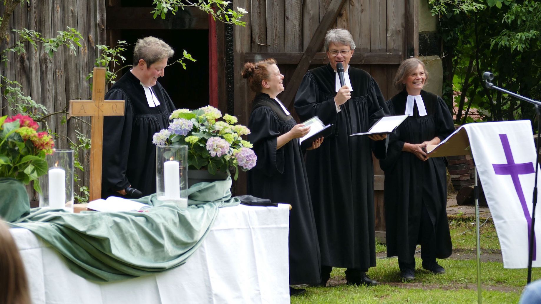 Vier Pfarrer und Pfarrerinnen vor Scheune am Altar